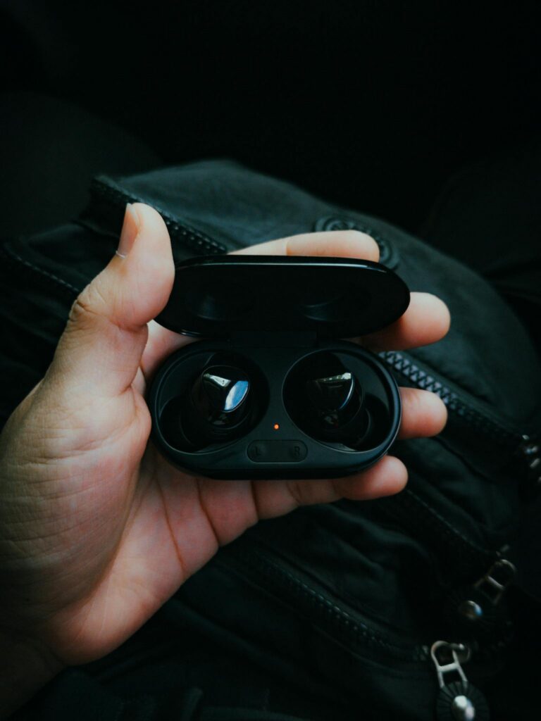 A person holds a pair of wireless earbuds inside their charging case, set against a dark background.